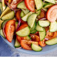 cucumber tomato salad in a serving bowl with spoons with recipe name at the bottom