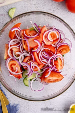 sliced cucumber, wedged tomatoes, and sliced red onion in a glass mixing bowl