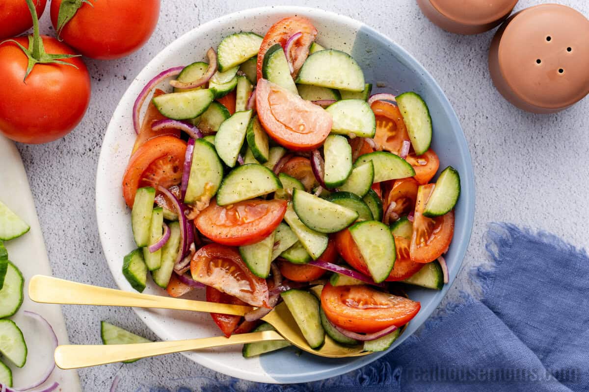 looking down at a serving bowl of cucumber tomato salad with serving spoons