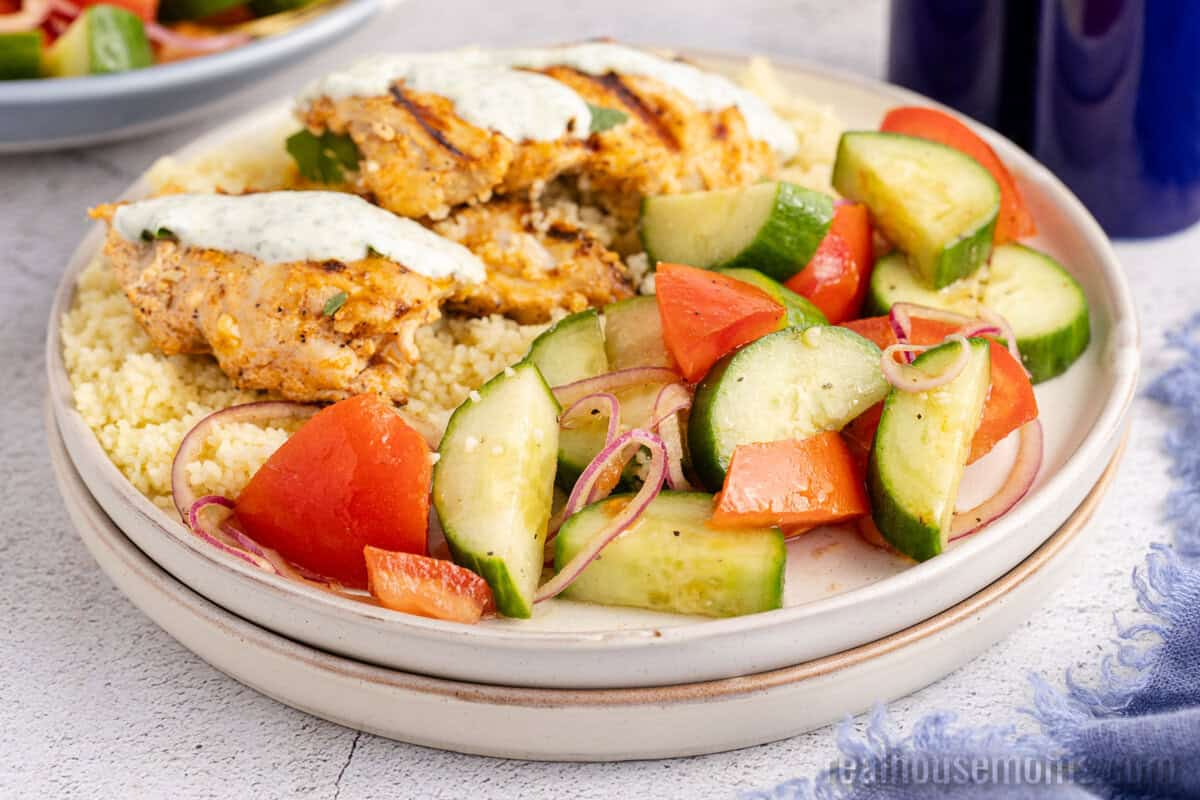 cucumber tomato salad on a plate with couscous and harissa chicken