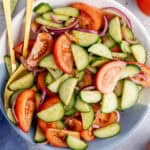 square image of cucumber tomato salad in a serving bowl with gold spoons resting on one side