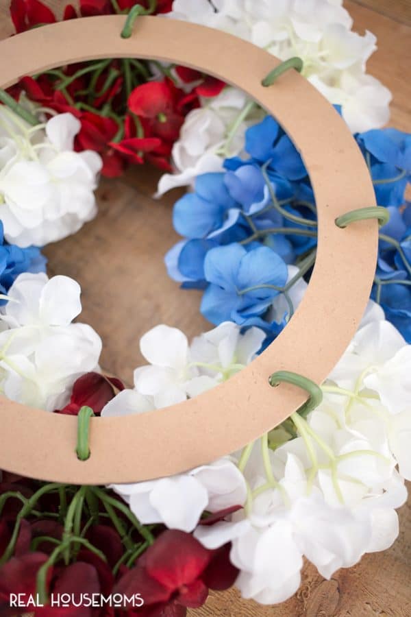 Hydrangea stems pushed through holes in floral craft ring and wrapped around to secure them for DIY Patriotic Wreath!
