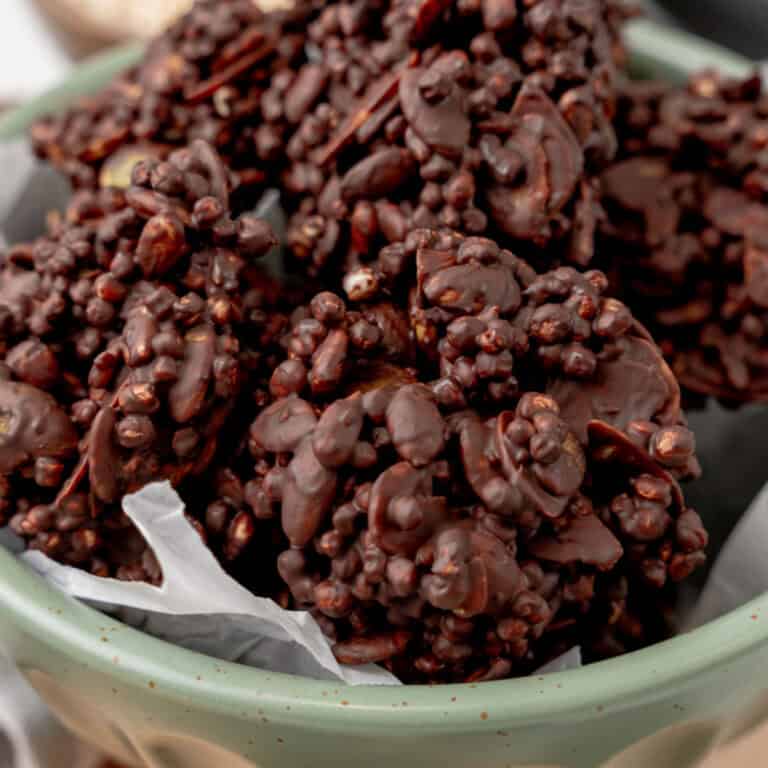 square image of dark chocolate keto clusters in a green bowl lined with parchment paper
