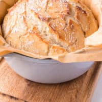 dutch oven bread in the pot with parchment paper and recipe name at the bottom