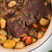 close up of pot roast in adtuch oven with potatoes and carrots with recipe name at bottom