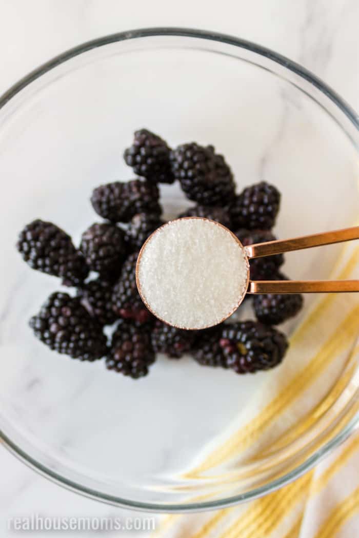 sugar being added to blackberries in a bowl