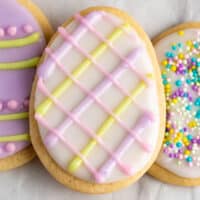 square image of an easter egg sugar cookie with white icing and pink, purple, and yellow criss-cross lines on top