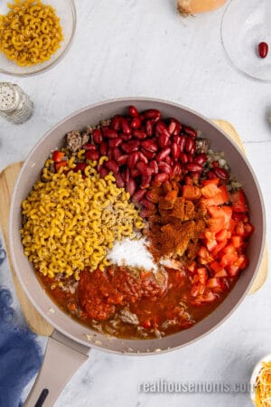 water, tomato sauce, diced tomatoes, kidney beans, elbow macaroni, and seasonings add to the skillet of ground beef