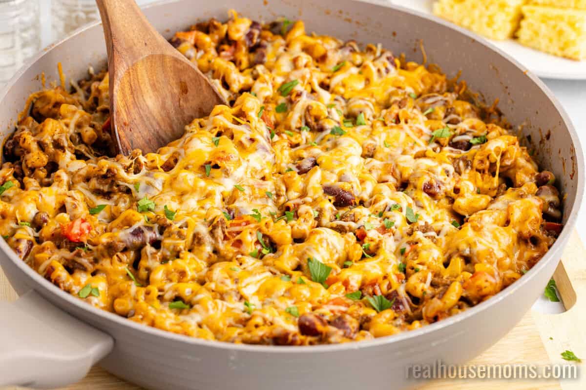 wooden spoon resting in a skillet of chili mac topped with chopped parsley