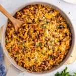 square image looking down at a skillet of chili mac skillet dinner with a wooden spoon