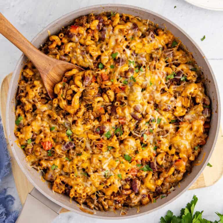 square image looking down at a skillet of chili mac skillet dinner with a wooden spoon