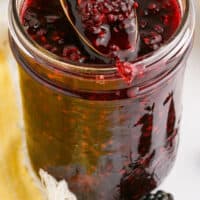 spoonful of easy homemade blackberry sauce over a mason jar with recipe name at the bottom