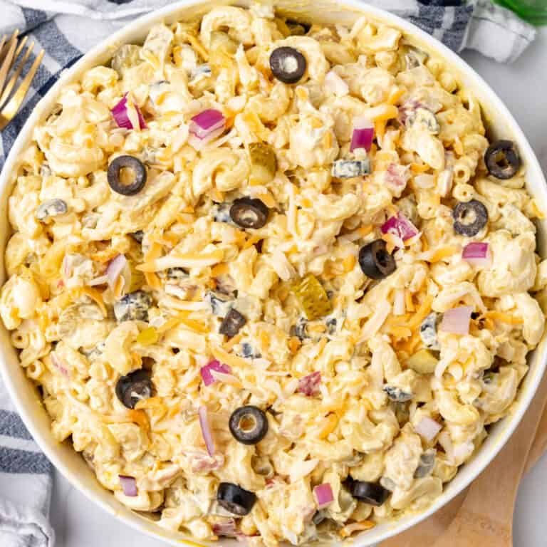 square image of macaroni salad with olives and pickles in a serving bowl