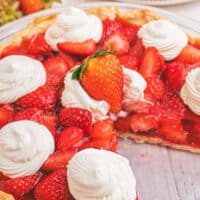 image of easy strawberry pie recipe topped with dollops of whipped cream with a side taken out. On top of the image is the title of the post in blue and black lettering