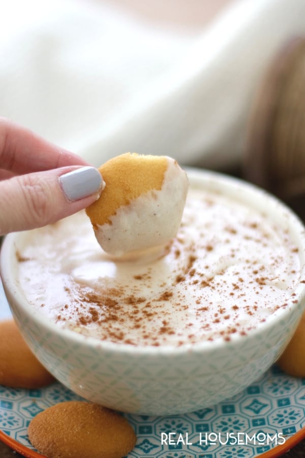 A cookie being dipped into Eggnog Cheesecake Dip