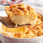 square image of a slice of eggnog french toast bake on a wooden spatula over the baking dish