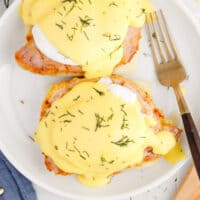 looking down at eggs benedict on a plate with a fork with recipe name at the bottom