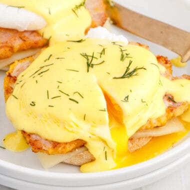 square image of eggs benedict with egg cut open to let the yolk run out