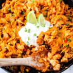 square image of enchilada pasta in a cast iron skillet with a wooden spoon