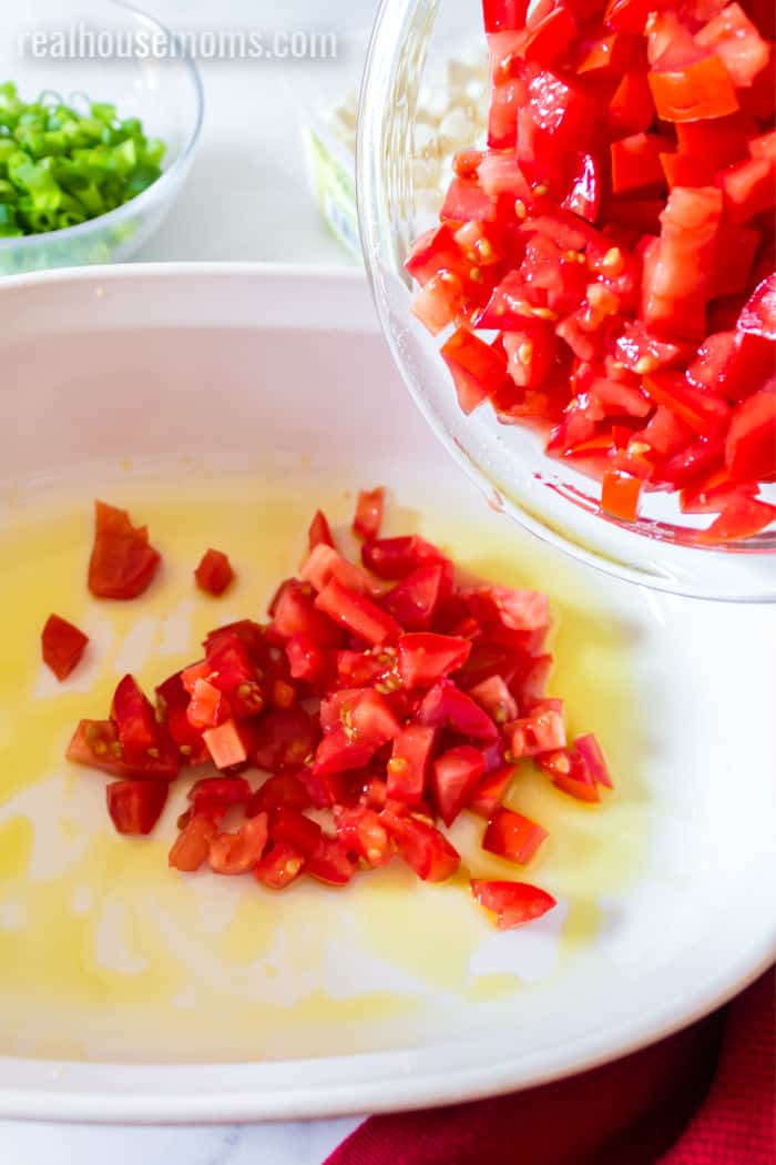 tomato being added to olive oil in a casserole dish