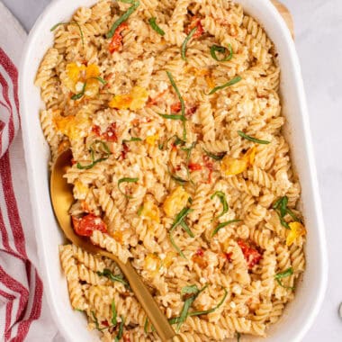 square image of feta pasta recipe in a baking dish with a serving spoon