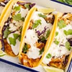square image of fish tacos in a serving dish with lime wedges