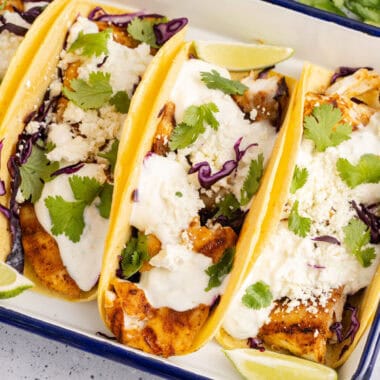 square image of fish tacos in a serving dish with lime wedges