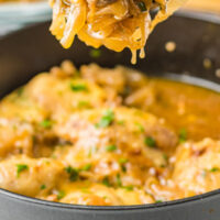 french onion chicken thigh on a spoon over the skillet with recipe name at the bottom