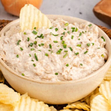 square image of french onion dip in a serving bowl with a chip stuck into the dip