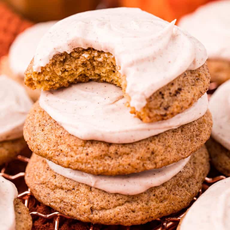 square image of frosted pumpkin snickerdoodles in a stack with a bite taken out of the top cookie