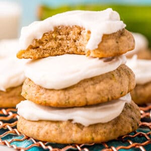 square image of frosted zucchini cookies stacked up with a bite taken from the top cookie