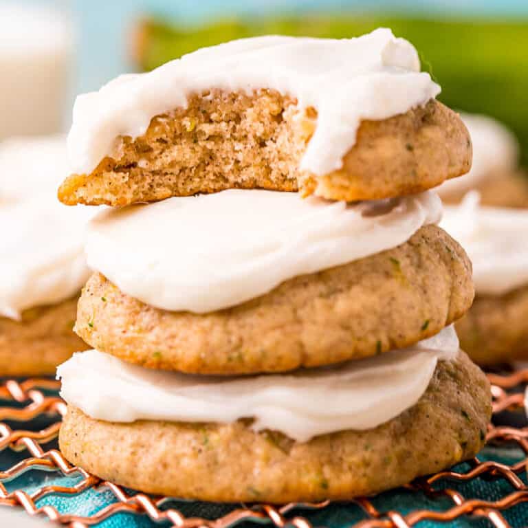 square image of frosted zucchini cookies stacked up with a bite taken from the top cookie