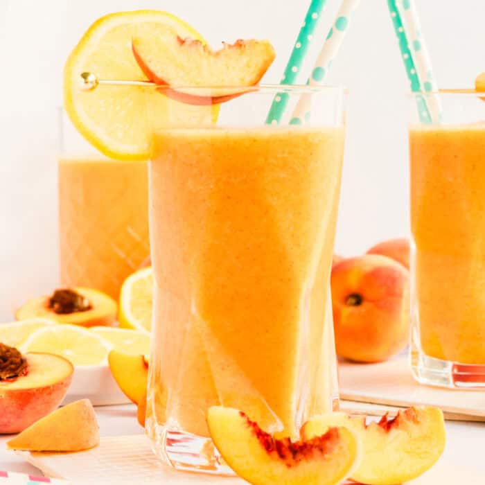 square image of frozen peach lemonade in a glass garnished with a peach and lemon slices