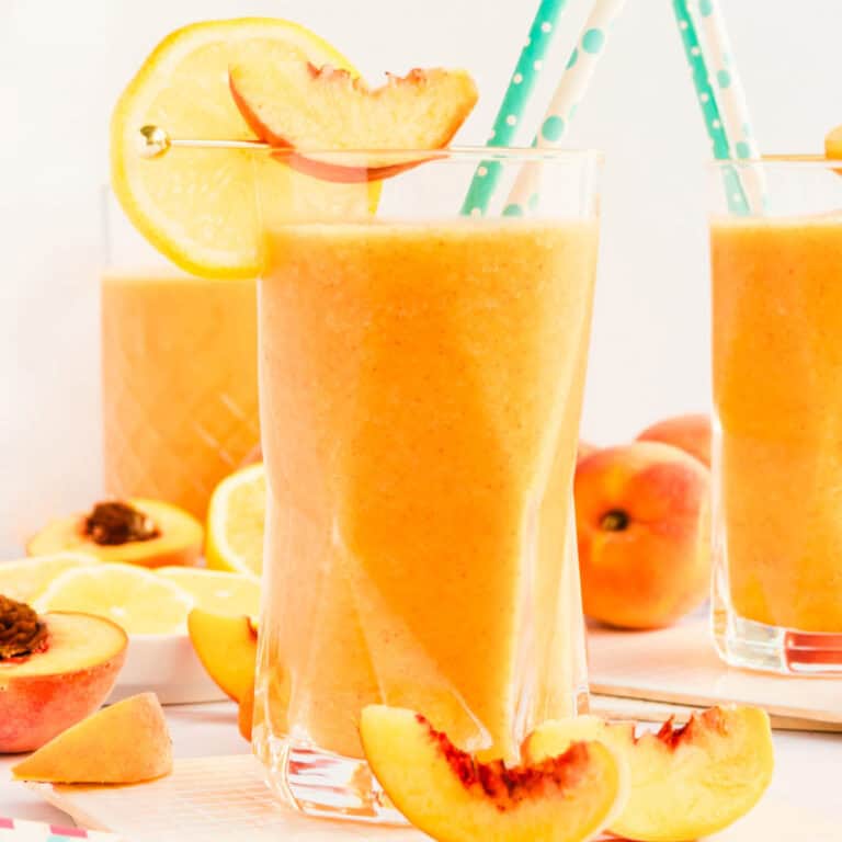 square image of frozen peach lemonade in a glass garnished with a peach and lemon slices