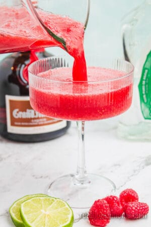 blended raspberry margarita being poured into a cocktail glass