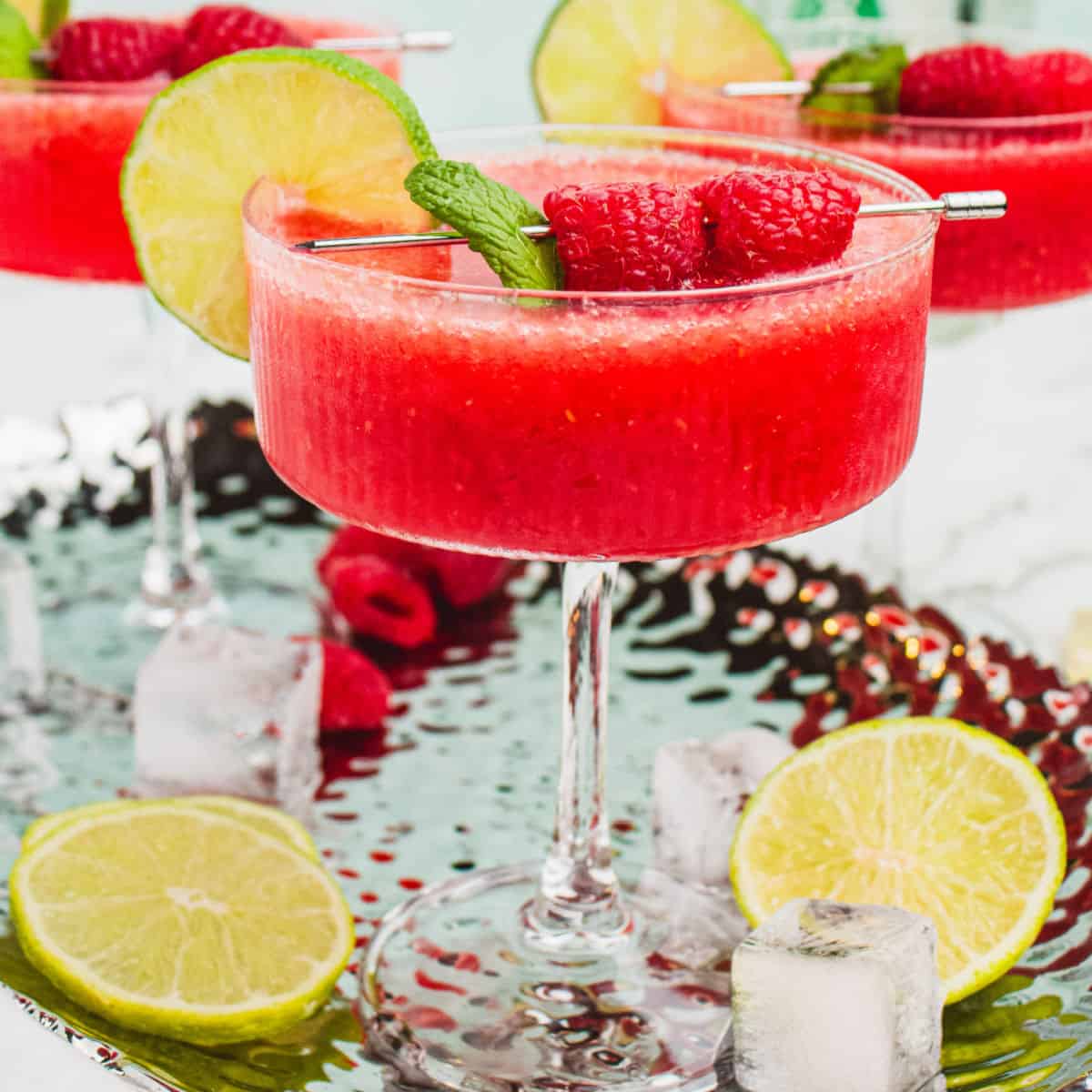 square image of a frozen raspberry margarita garnished with a lime slice and fresh raspberries on a cocktail pick