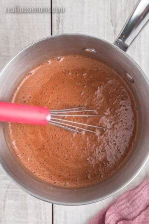 whisk resting in a pot of cocoa powder, brown sugar, cornstarch, and milk that's been whisked together
