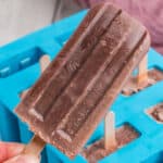 square image of a hand holding a fudgesicle with popsicle mold in the background