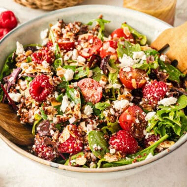 square image of fully loaded raspberry salad in a serving bowl with wooden serving forks