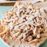 square image of funnel cakes on a plate topped with powdered sugar