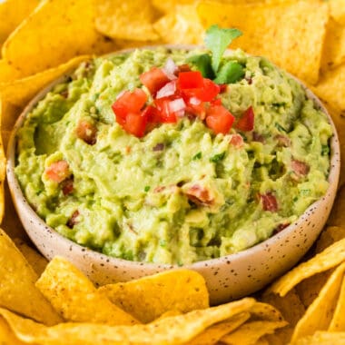 square image of garden fresh guacamole in a serving bowl surrounded by tortilla chips