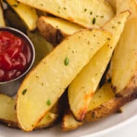 garlic ranch potato wedges and a cup of ketchup on a plate with recipe name at the bottom