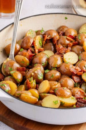angled view of german potato salad tossed with chopped parsley in a skillet with a serving spoon