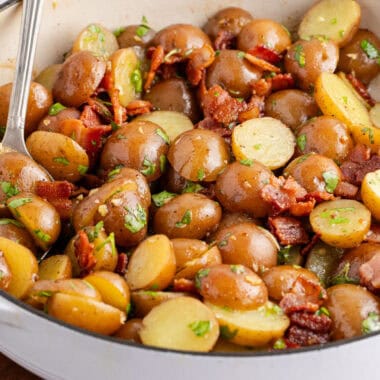 square image of german potato salad with a serving spoon in a white ceramic skillet
