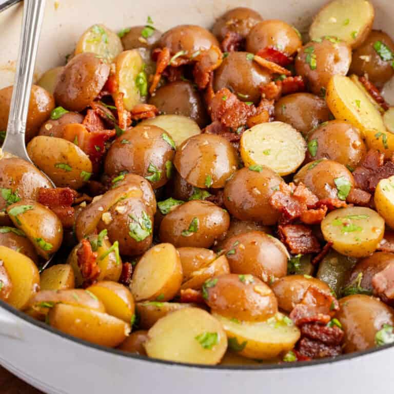 square image of german potato salad with a serving spoon in a white ceramic skillet