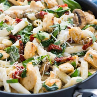 goat cheese chicken penne pasta in a skillet with muchrooms, basil, parmensa cheese, and sun-dried tomatoes