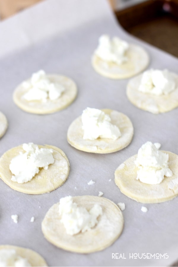 Raw puff pastry dough cut into circles on a baking sheet with goat cheese to make Goat Cheese and Honey Bites 