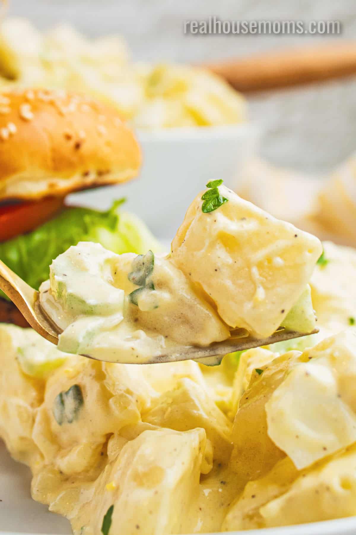 forkful of grandma's best potato salad recipe over a plate with a burger and potato salad