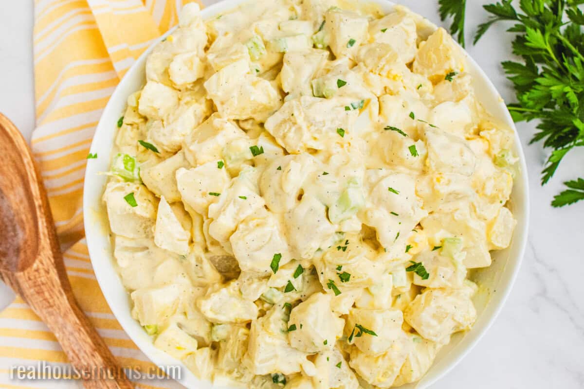 grandma's best potato salad in a serving bowl next to a wooden spoon and fresh parsley