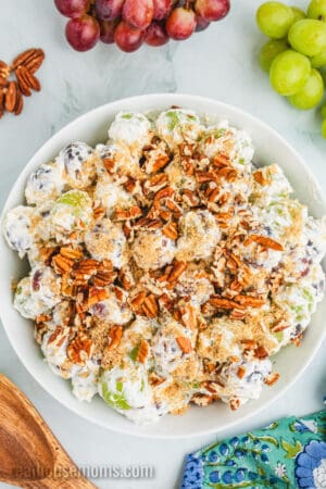 grape salad topped with brown sugar and chopped pecans in a white serving bowl